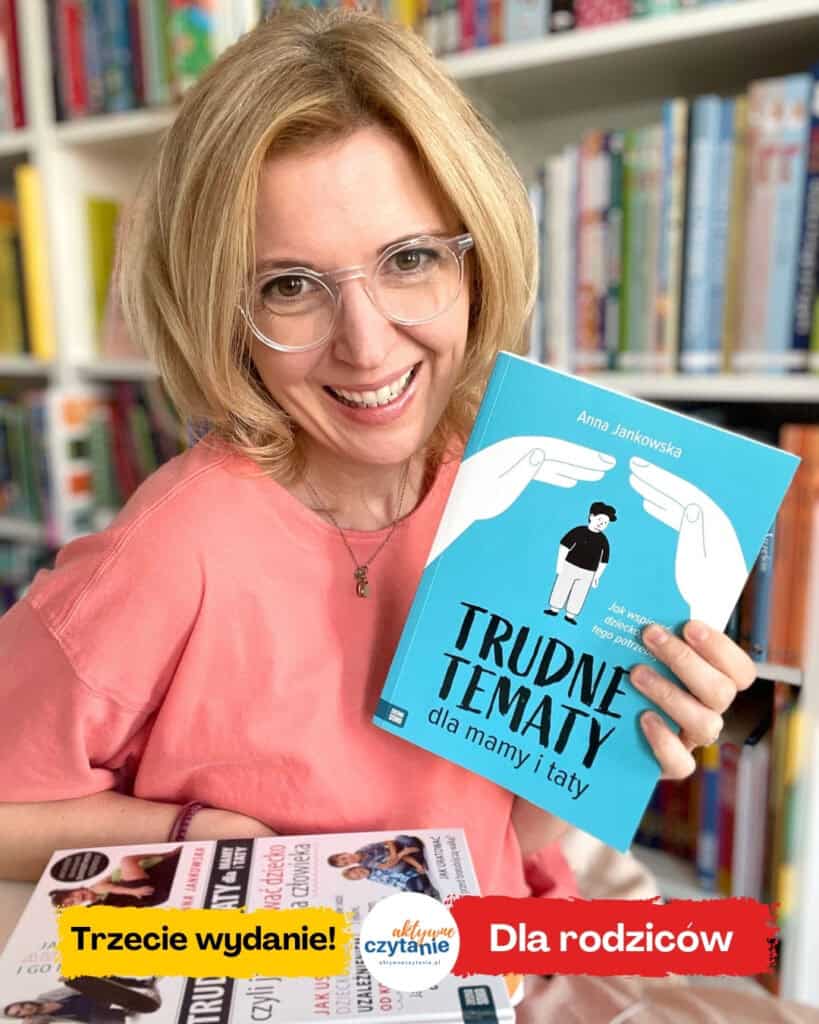 A woman holding up a a blue book „trudne tematy dla mamy i taty’