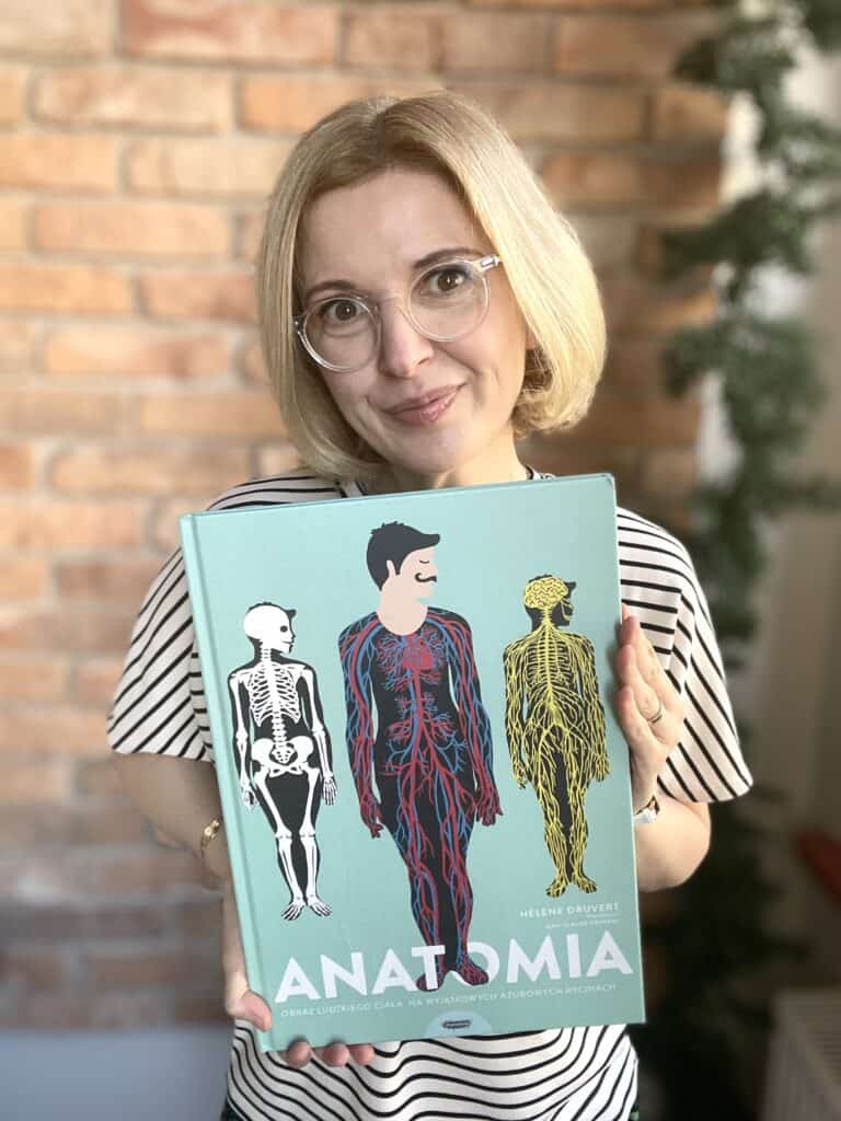 Zdjęcie kobiety z książką o anatomii, promującą aktywne czytanie i rozwijanie wiedzy humanistycznej.