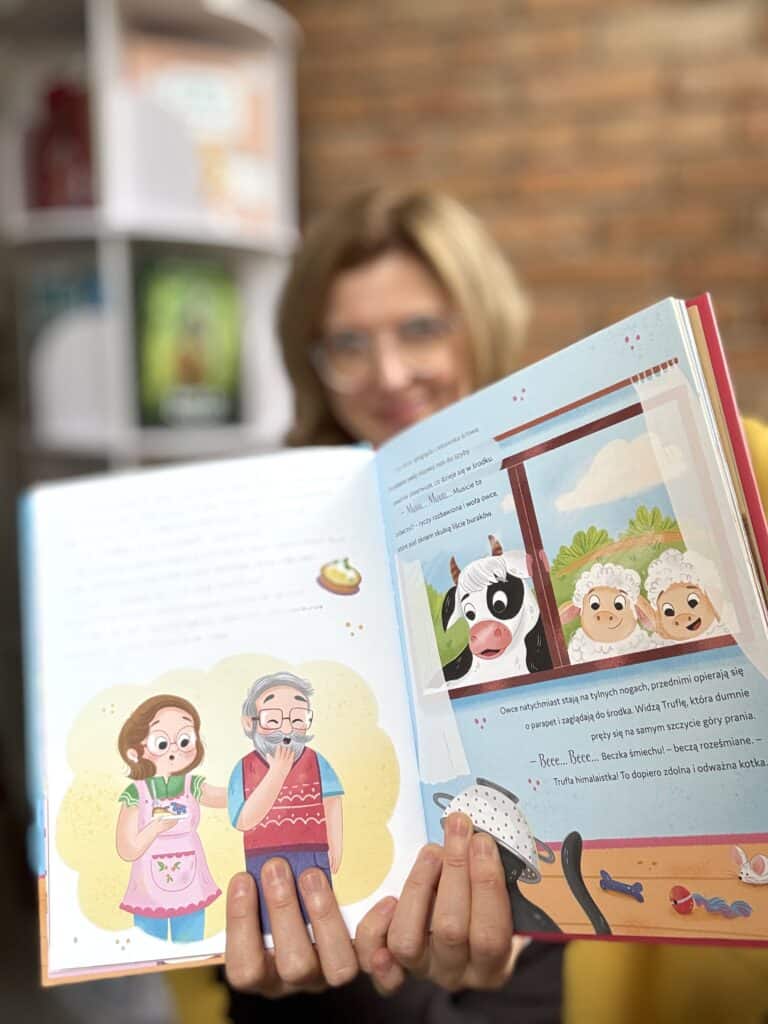 Kobieta trzyma otwartą książkę z ilustracjami dla dzieci, w tle regał z książkami.