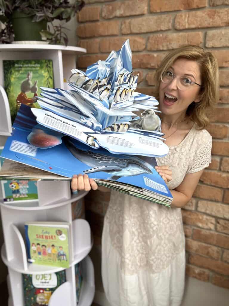 Kobieta trzyma ogromny stos książek 3D z ruchomymi elementami i okienkami.