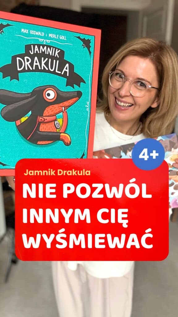 Uśmiechnięta kobieta w okularach trzyma okładkę książki „Jamnik Drakula” z ilustracją jamnika w pelerynie, a na czerwonym pasku napis „Nie pozwól innym cię wyśmiewać