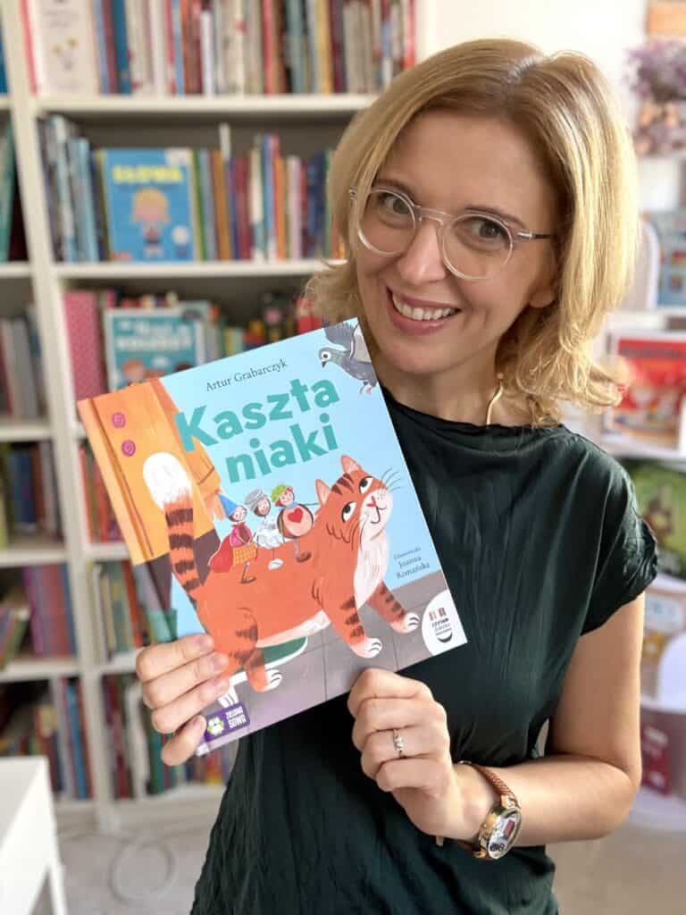 Kobieta trzymająca książkę Kaszta niaki w bibliotece dla dzieci.