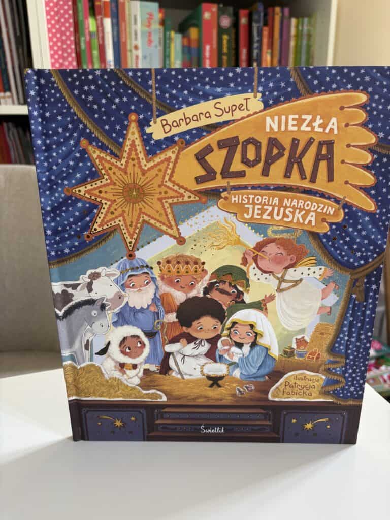 Okładka książki „Niezła szopka. Historia narodzin Jezuska” Barbary Supeł: kolorowe dzieci w szopce pod gwiazdą, z aniołem, zwierzętami i Świętą Rodziną Hmm, the instructions say no period at the end, and the text should be a single sentence up to 120